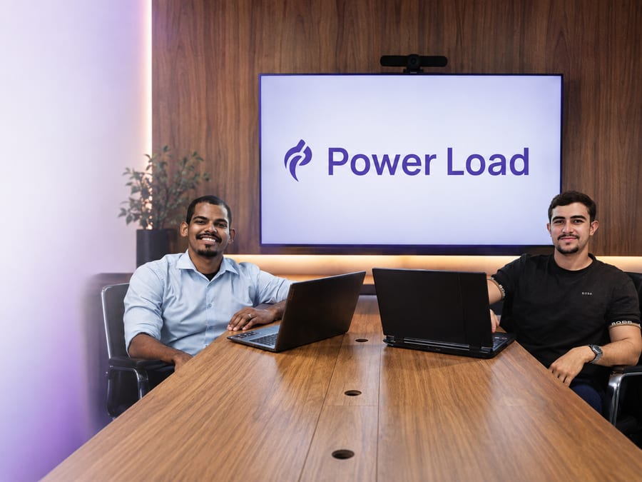 Equipe da Power Load reunida na sala de reuniões do estúdio, com a marca exibida na tela
